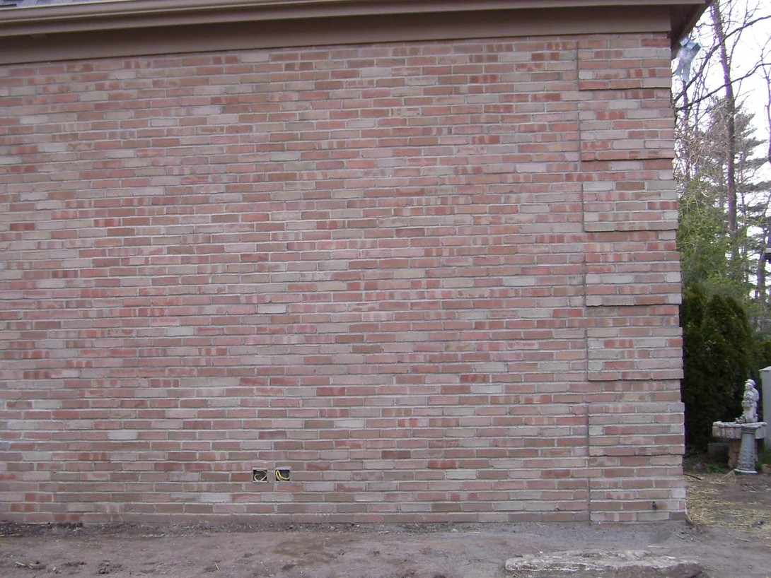 The same addition wall finished in 2009, the brick now a mixed rose, buff and cream range running unbroken to the corner, the ground still bare from the build