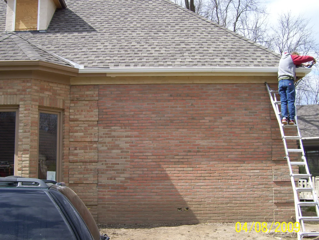 The addition wall mid-job in 2009, its brick reading distinctly redder than the buff brick around the bay window to the left, with an applicator on a ladder at the eaves