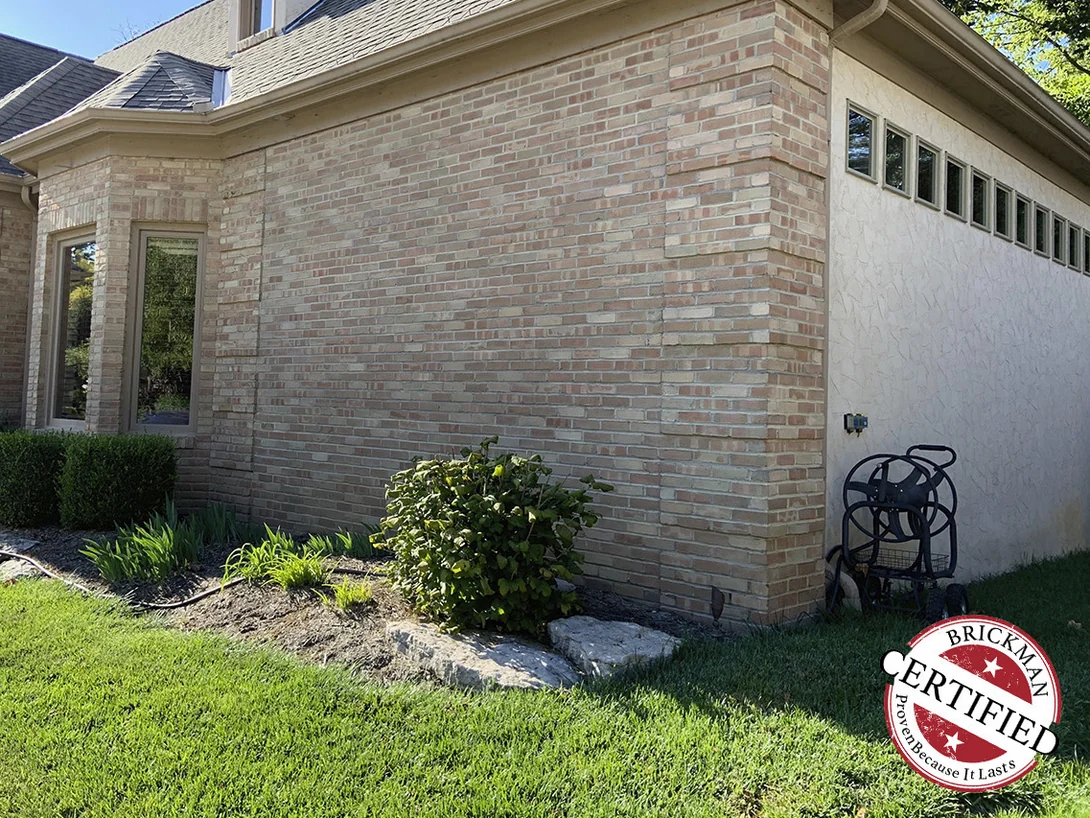 An outside corner of the house in 2019 running from the planting bed to the eaves, the brick evenly blended on both faces where it meets the stucco garage wall