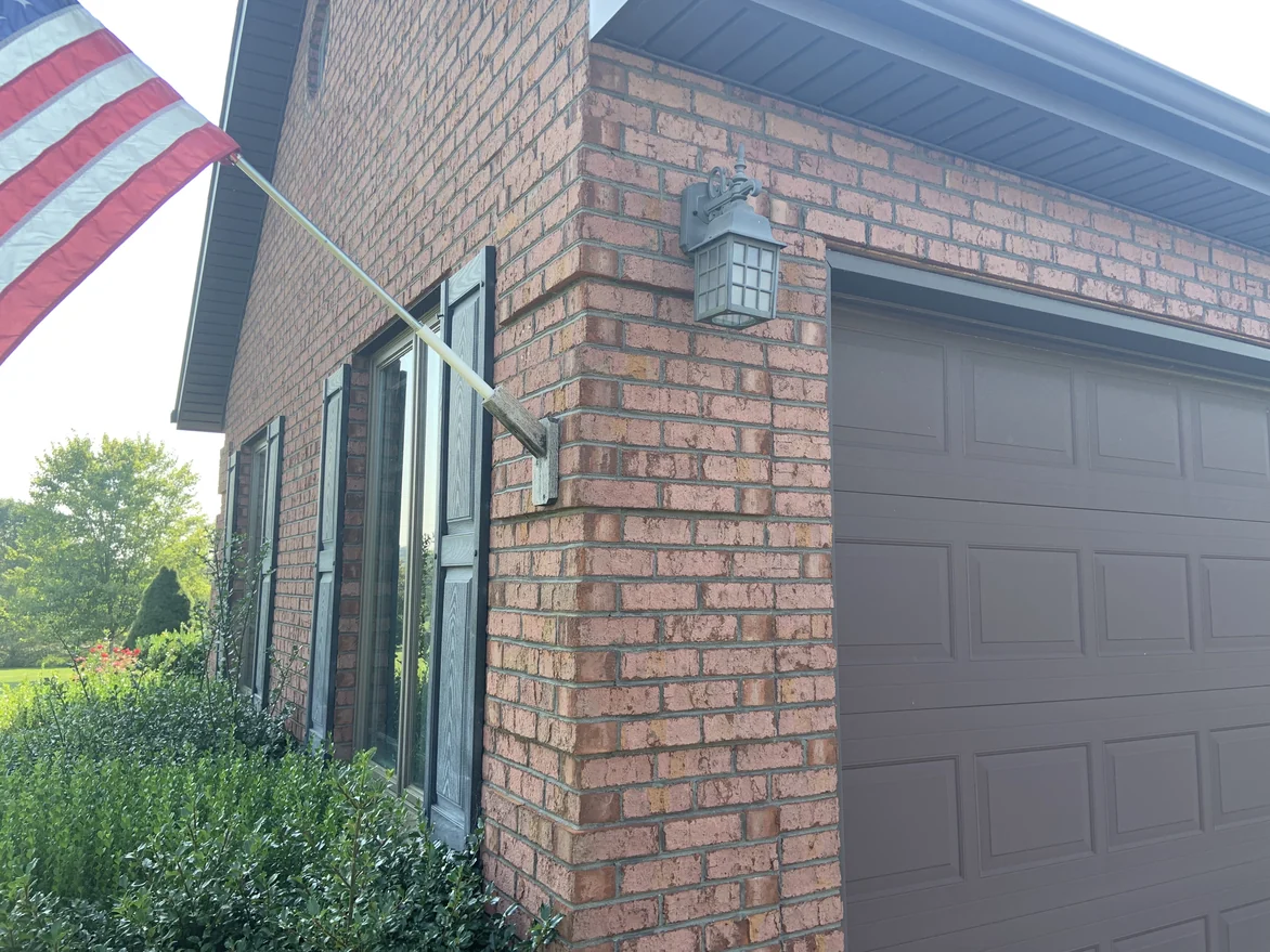 An outside corner of the garage in 2019, a carriage lamp on the pier and the brick evenly ranged across both faces