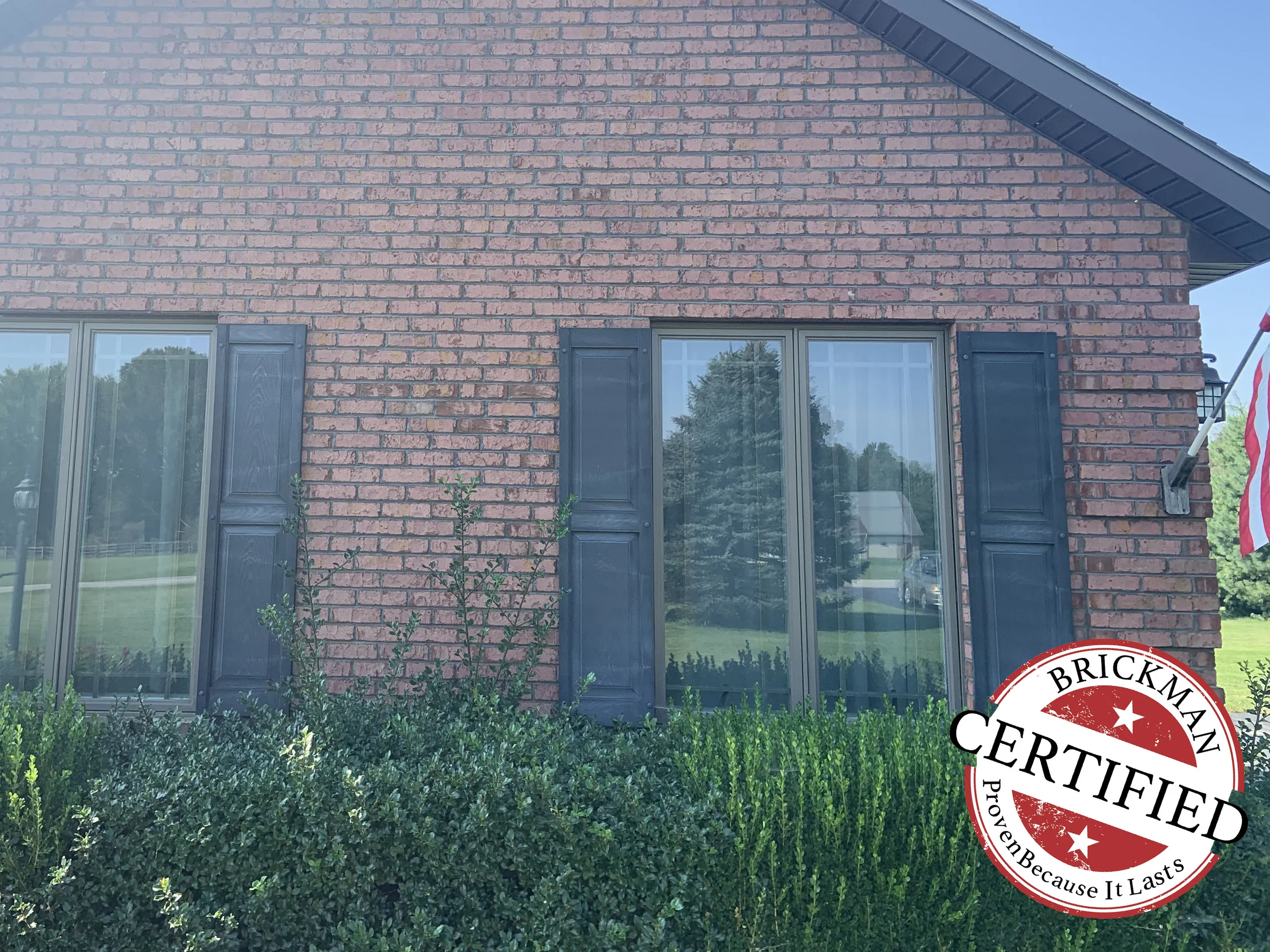 The gable end in 2019, two shuttered windows in brick that runs as one pink, tan and cream range, with the certification stamp at the corner