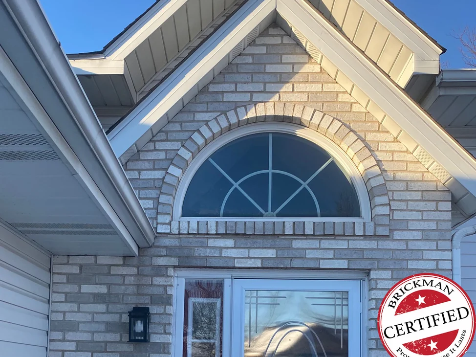 The front entrance of the Hobart house in 2021, pale grey brick around the arched transom and the door under the gable, with the certification stamp in the corner
