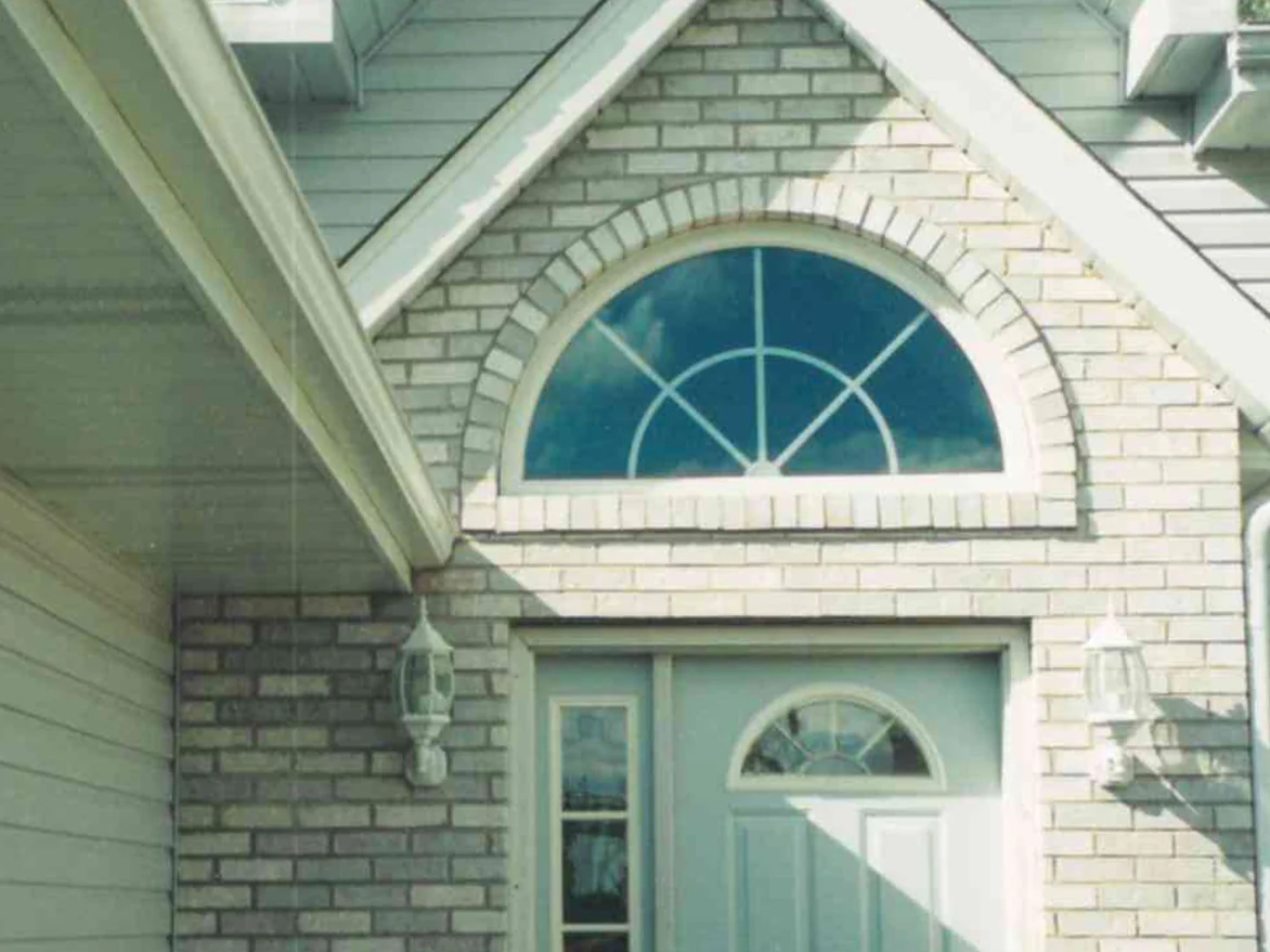 The front entrance of the Hobart house before staining, grey and tan brick around an arched transom window under the gable, the light and dark units unevenly spread across the wall