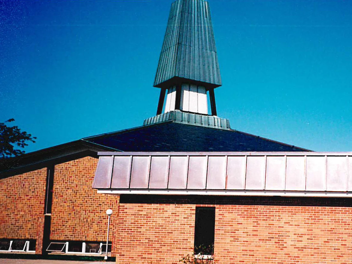 The 1998 addition in even red brick meeting the older tan and multicolored brick of the church at the left, the copper clad spire above