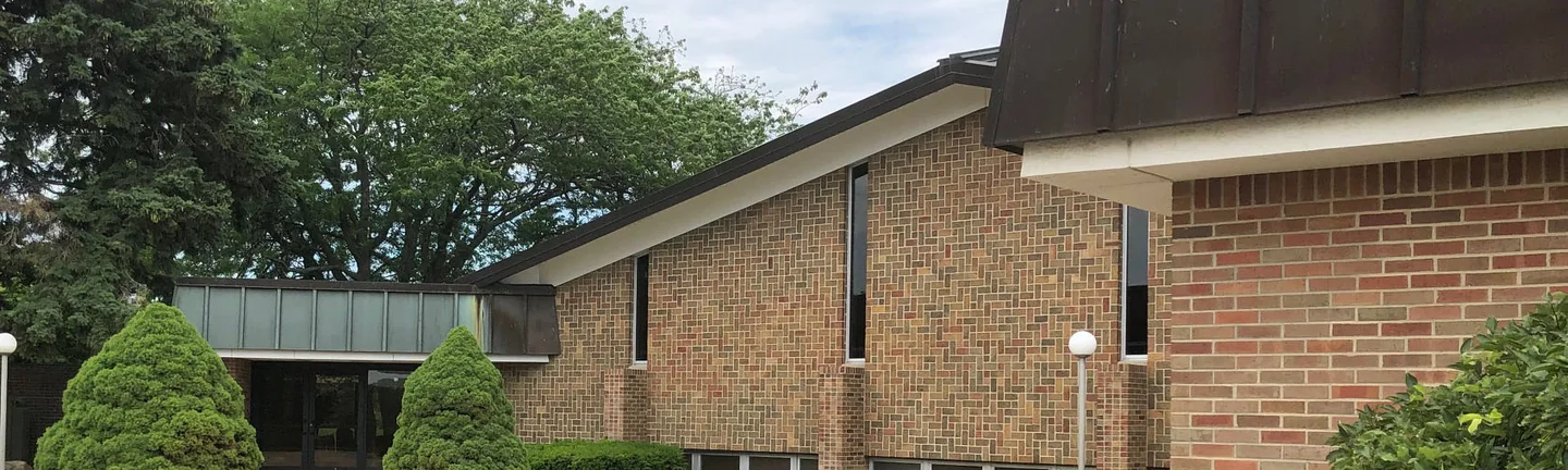 The church across its courtyard in 2019, the roofline running from the entrance link to the brick pier at the corner