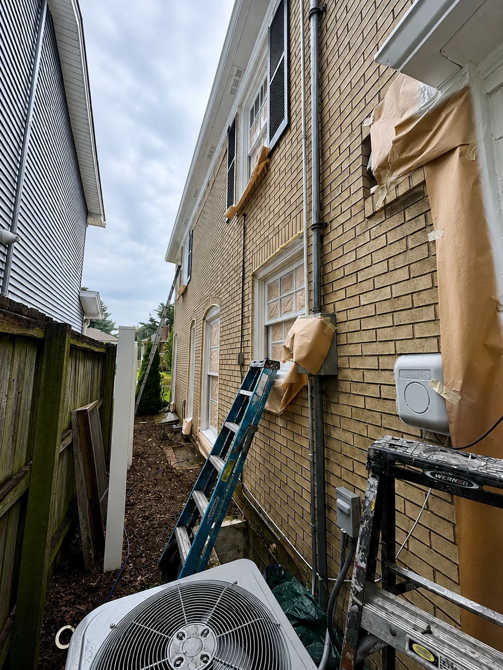 A buff brick side wall at close range, masking paper taped over the meter, the disconnect box and the window heads