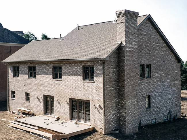 Rear of a newly built two-story house, its brick patchy gray in two mismatched shades, deck still under construction