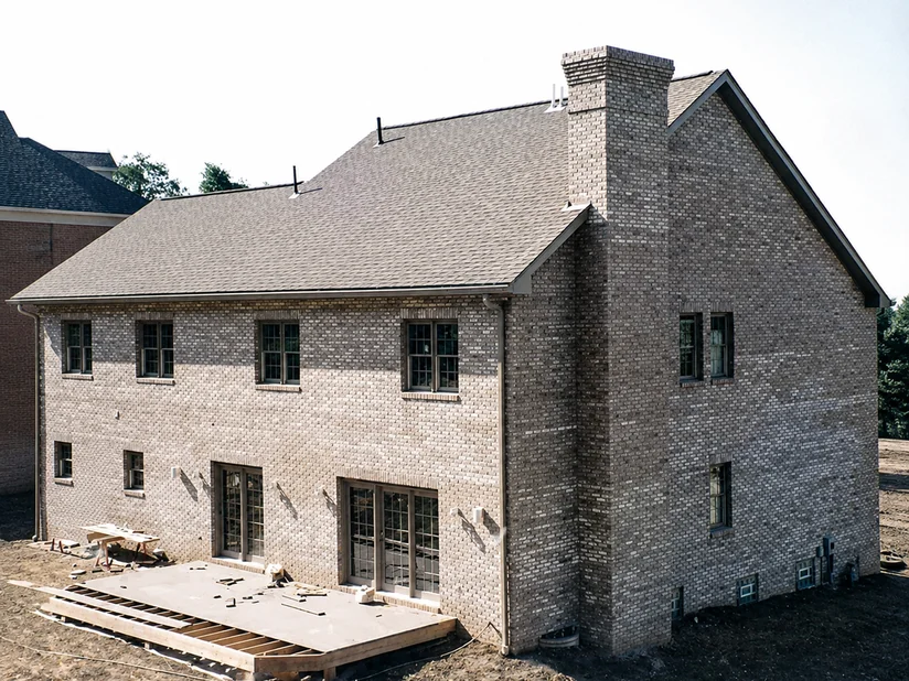 Rear of a newly built two-story house, its brick patchy gray in two mismatched shades, deck still under construction