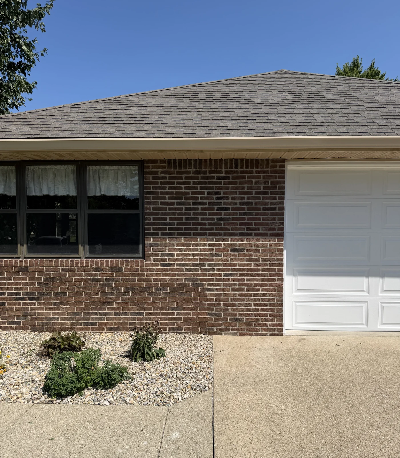 A stained brick wall between a front window and a white garage door in 2026, the reds and browns one even range