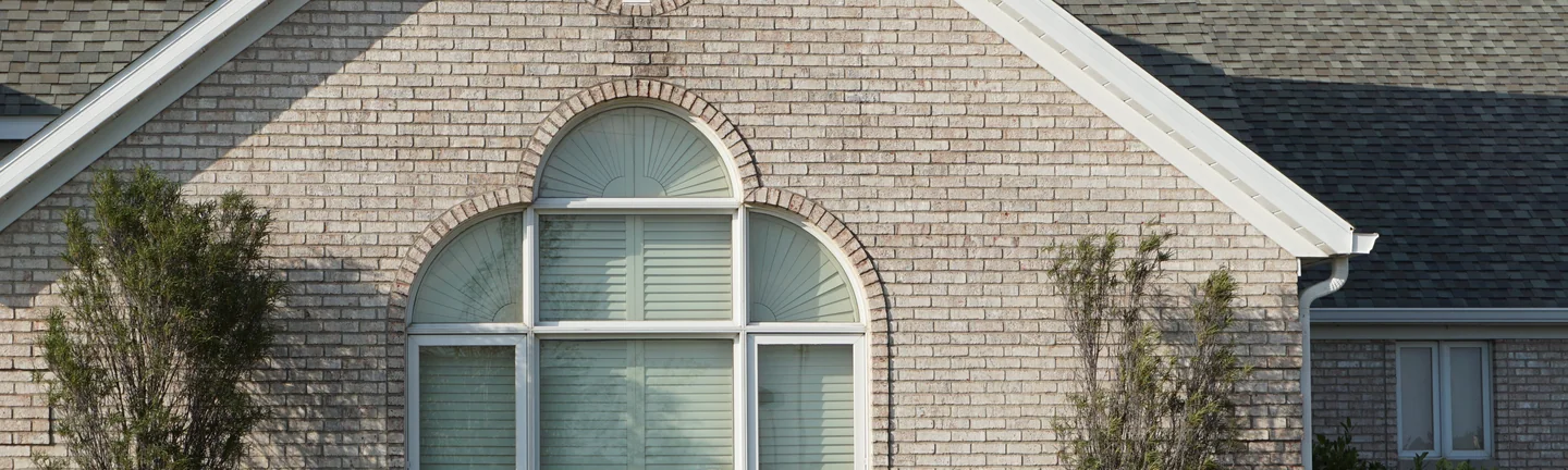 The front gable of the house in 2019, its arched window ringed with brick that reads as one cream and grey range