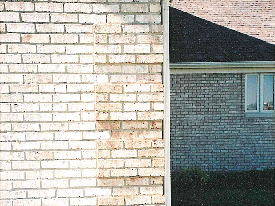 A cream brick wall in 2003 with a broad band of tan and pink flecked brick running down the middle of it, the corner and a shadowed wing beyond