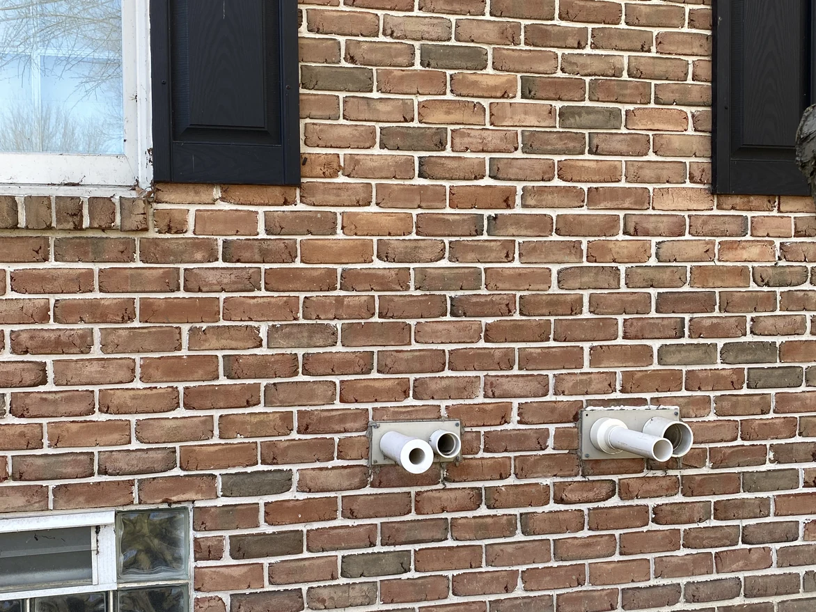 The brick at close range in 2021, units carrying a mix of red, tan and grey over pale mortar, with two vent pipes through the wall
