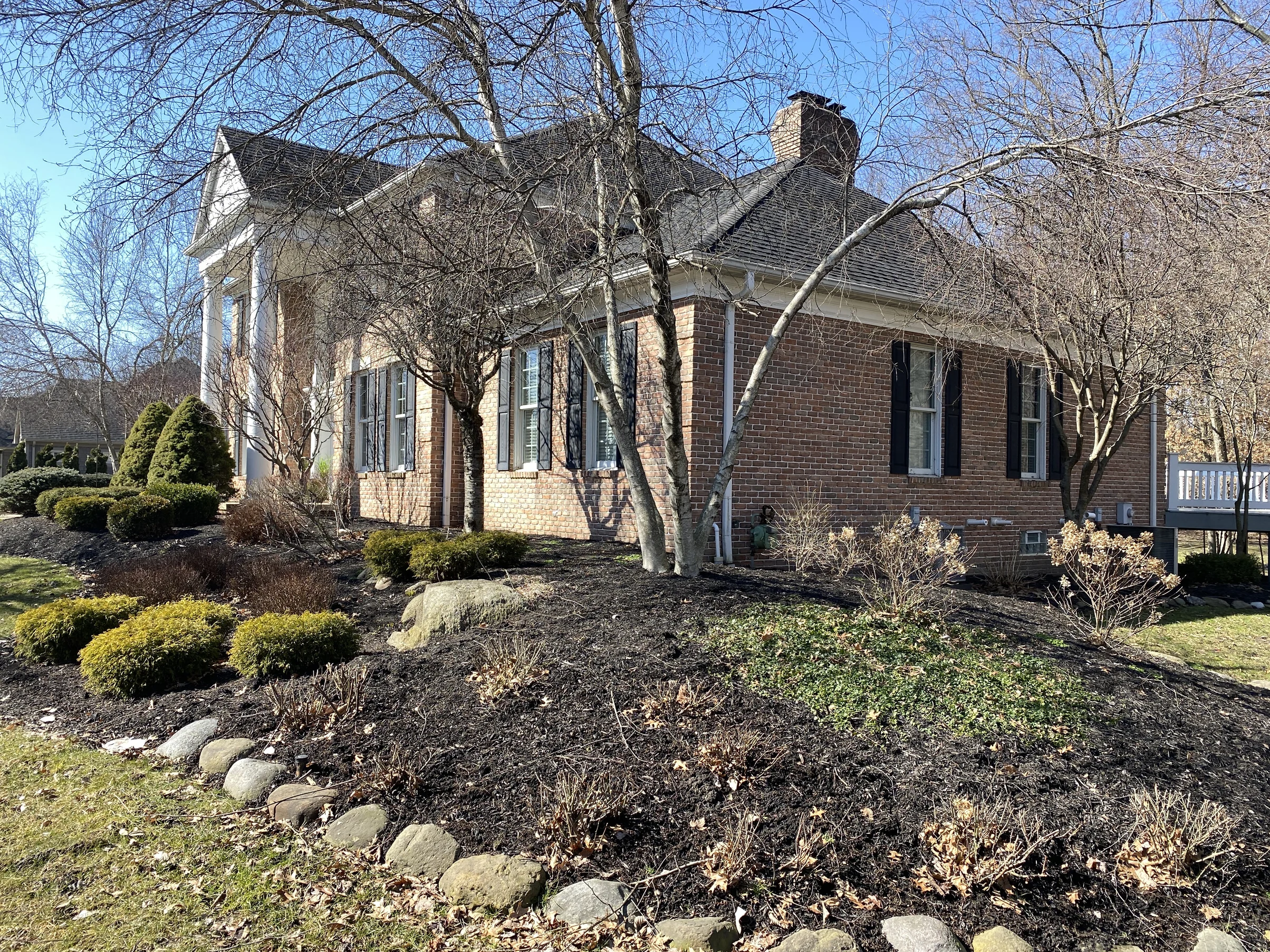 The house in 2021 seen from the front corner, red brown brick running the length of the side elevation to a chimney on the ridge and a white portico at the far end