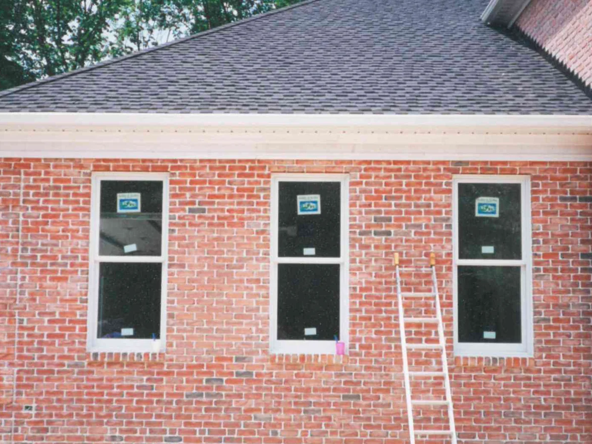 Three tall windows in a row in 1997, small stain cups sitting on two of the sills and an extension ladder standing against the brick between them