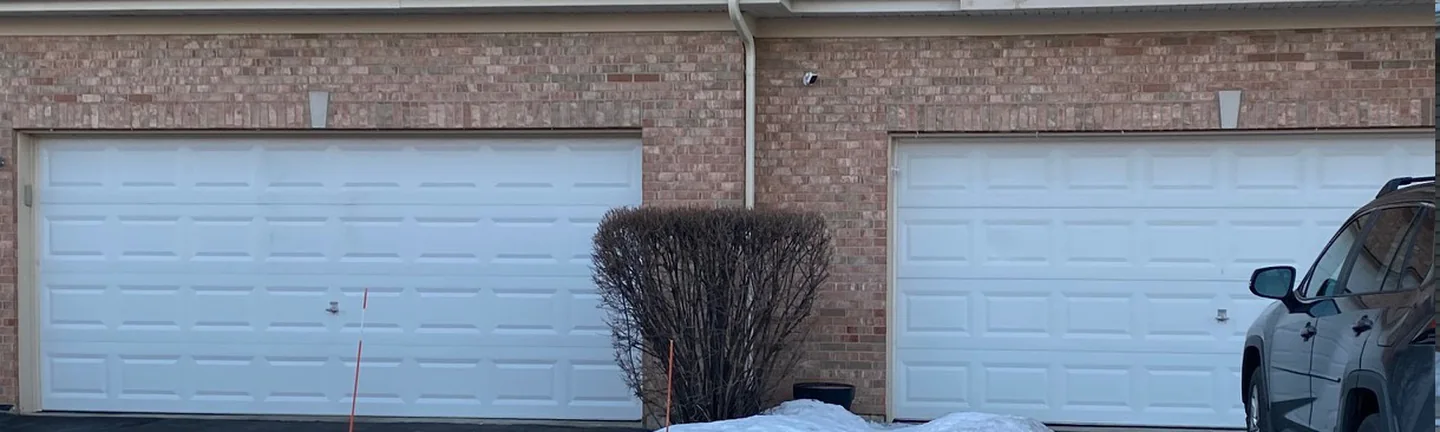 Two garage bays of the apartment row in 2019, brick running across both openings under tan siding