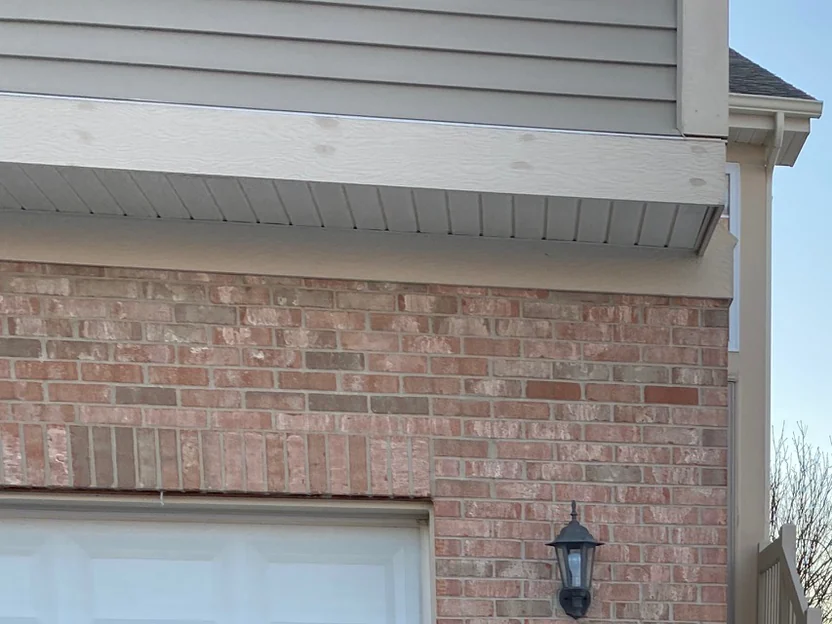 The wall over the same garage door in 2021, the end-set course above the opening carrying the same range as the field brick, a coach lamp on the corner pier