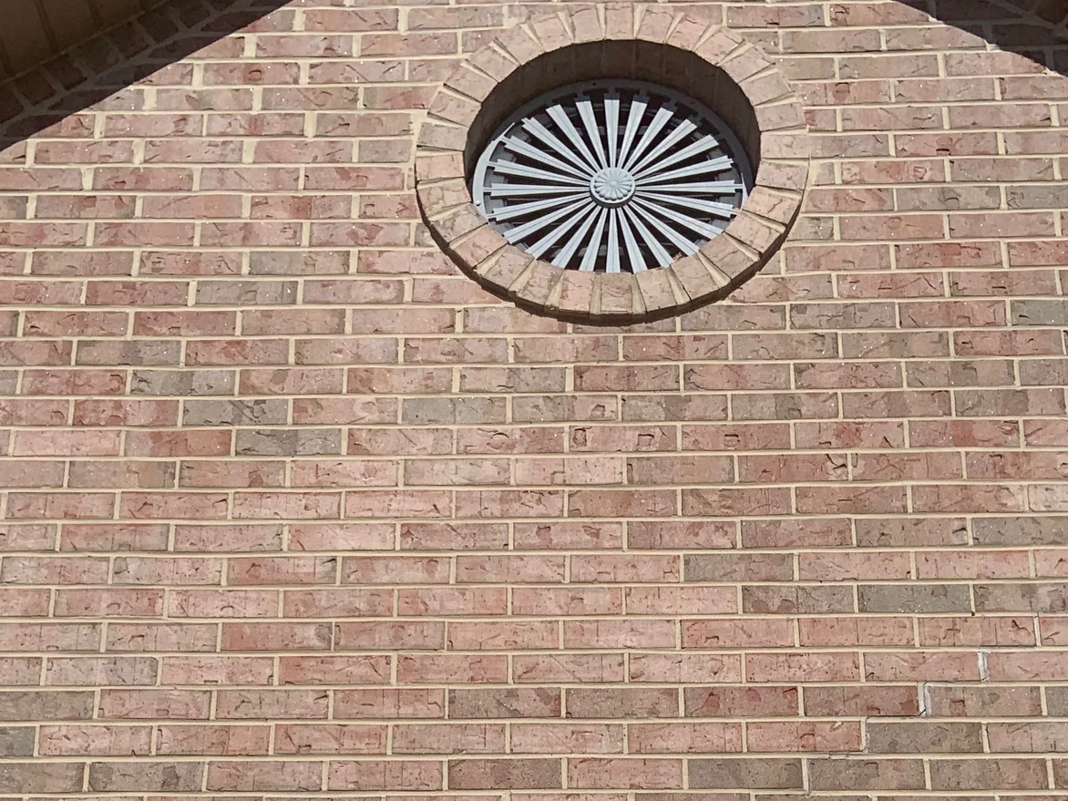 Close view of the gable brick in 2019, pale pink and buff units with a few soft greys around a round louvered vent set in a brick arch