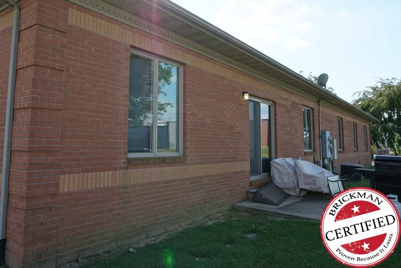 The office in 2019 from an outside corner, the wall running away in one even red brick with buff soldier bands above and below the windows, and the certification stamp at the corner of the frame