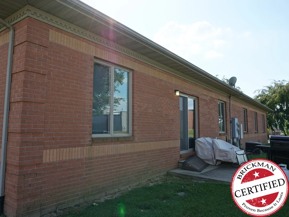 The office in 2019 from an outside corner, the wall running away in one even red brick with buff soldier bands above and below the windows, and the certification stamp at the corner of the frame