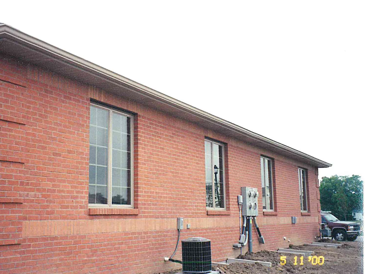 The side elevation later in 2000, the brick reading as one even red across the wall with a buff band at the base, the ground still bare soil and fresh concrete