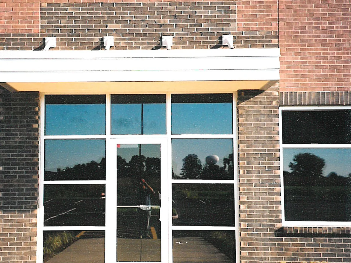 A glazed entrance under a flat canopy in 2003, the brick piers and the band above it a pale blotchy grey beside red field brick