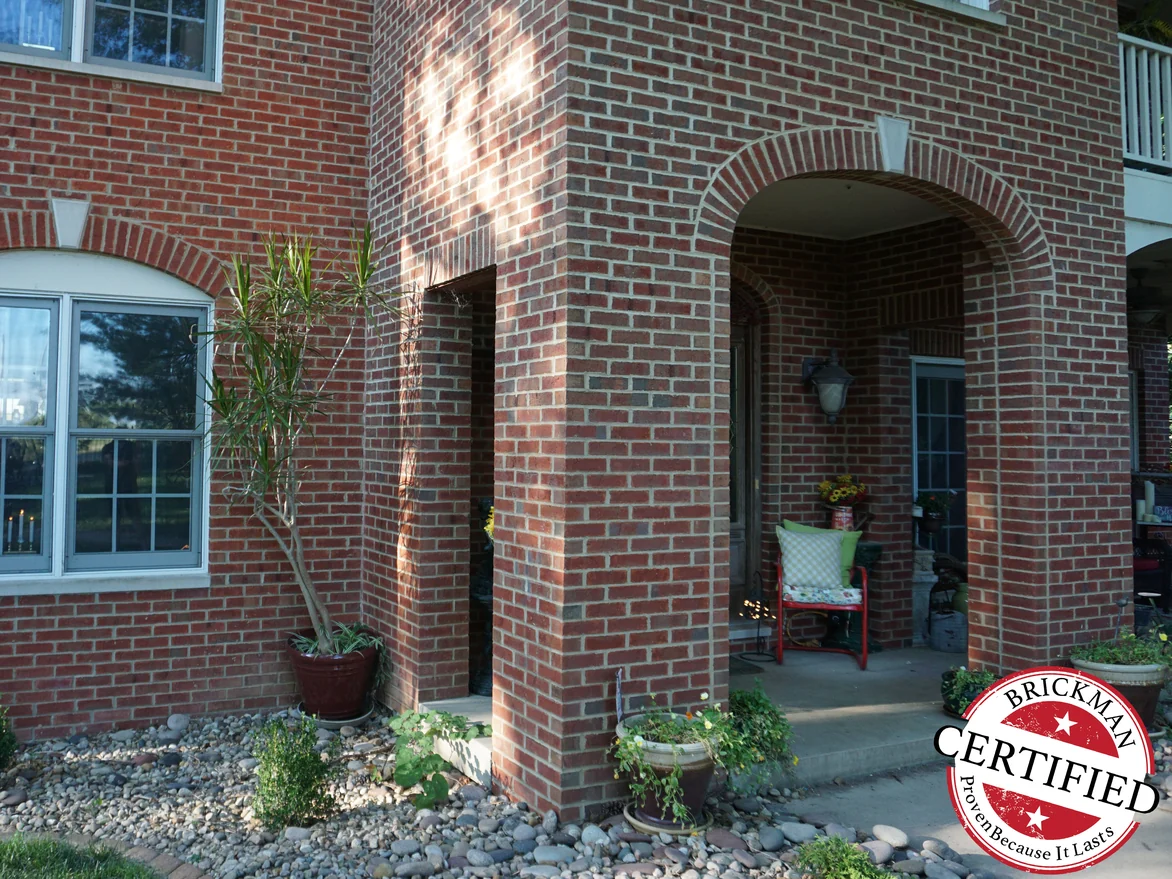 The arched entry and its outside pillar in 2019, the brick one even red range from the planting bed at the ground to the windows above