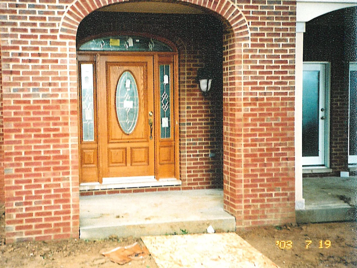 The arched front entry in 2003, the two brick pillars carrying the arch running a pale orange red with cream mortar joints, the ground around them still bare soil