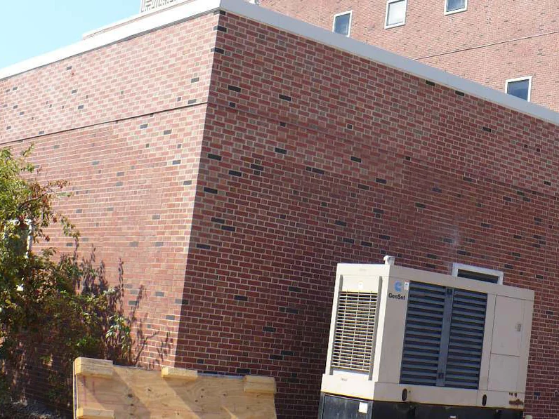 The same single-story corner in 2019, the generator still against the wall and the brick carrying dark units through every course