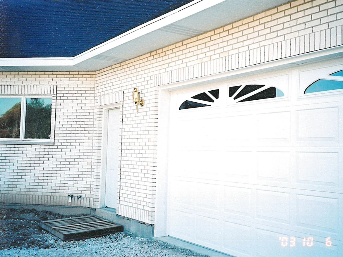 The garage end of the house in 2003, the ground still bare gravel, tan units scattered through the white brick around the door head