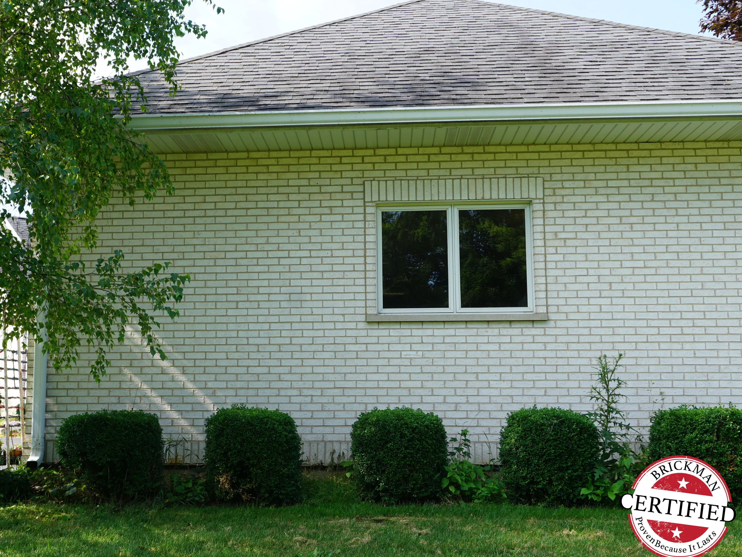 A side wall of the house in 2019 under its hipped roof, the white brick even across the whole elevation with clipped boxwood along the foot