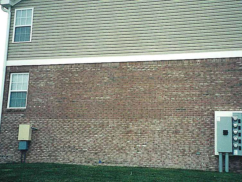 The side elevation of the apartment building in 2002, a band of brick under tan siding with a bank of electric meters at the far end, the units reading in patches of lighter and darker color