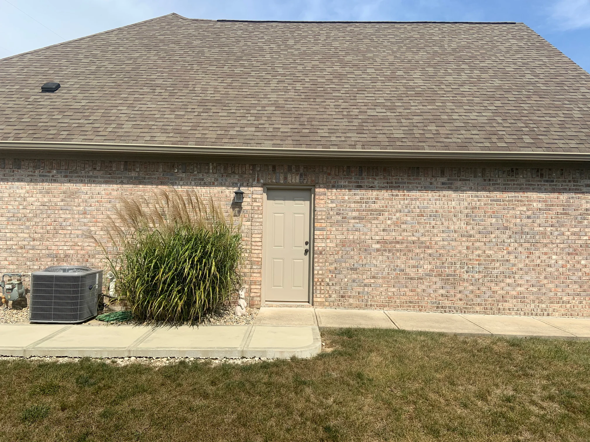 The side of the house in 2019 from the lawn, the brick reading as one tan and grey range from the footing to the eaves beside a service door