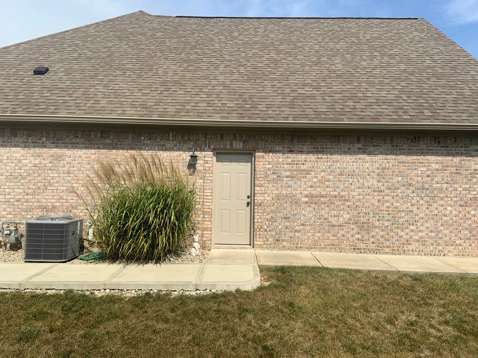 The side of the house in 2019 from the lawn, the brick reading as one tan and grey range from the footing to the eaves beside a service door.