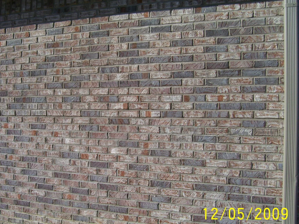 A brick wall in 2009 under a deep overhang with a downspout at the right, the courses mixing tan, cream and dark grey units