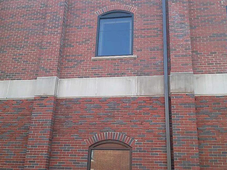 The same wall in 2003 after staining, red brick with scattered dark headers running both above and below the limestone band, past an arched window to an arched doorway