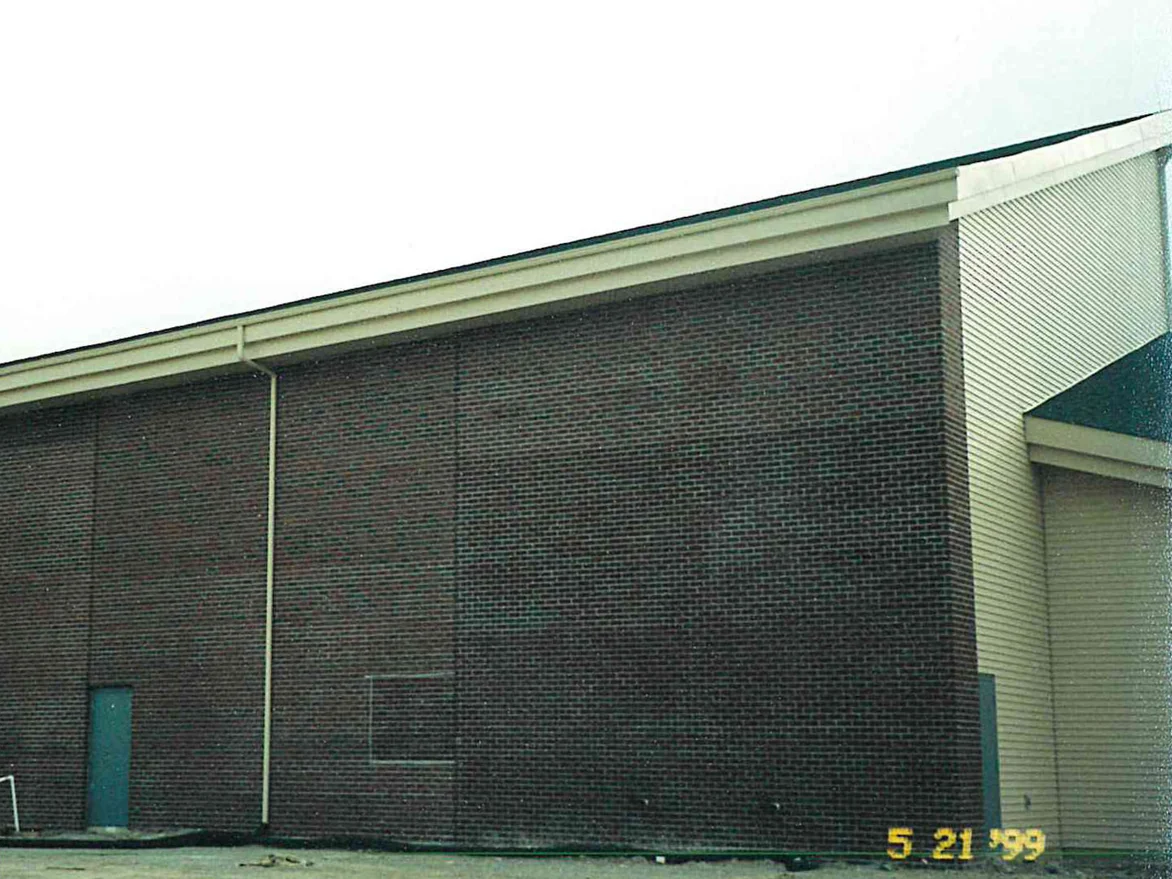 The long side elevation of the church in 1999, the brick a dark uneven maroon and brown under a shallow sloping roof, with a camera date stamp at the foot of the wall
