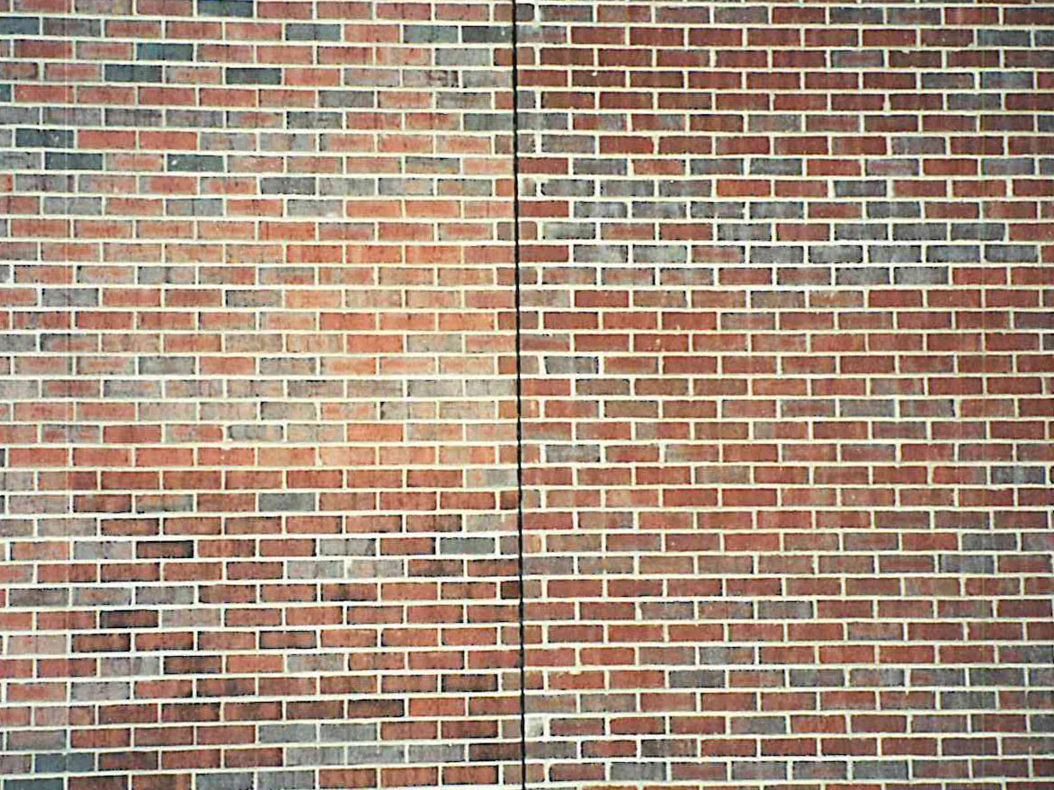 The stained wall in 1999 either side of a vertical control joint, the brick a worked blend of reds, tans and dark greys under pale mortar