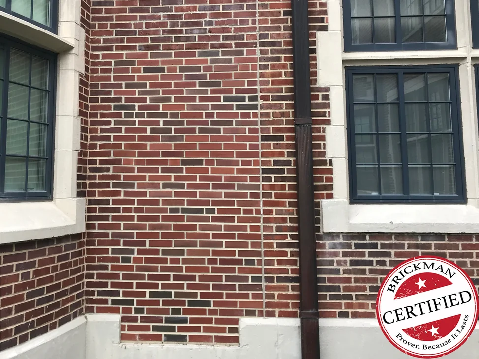 The fill-in panel between the bay window and the downspout in 2020, its brick carrying the same red and dark units as the original wall around it, with the certification stamp in the corner.