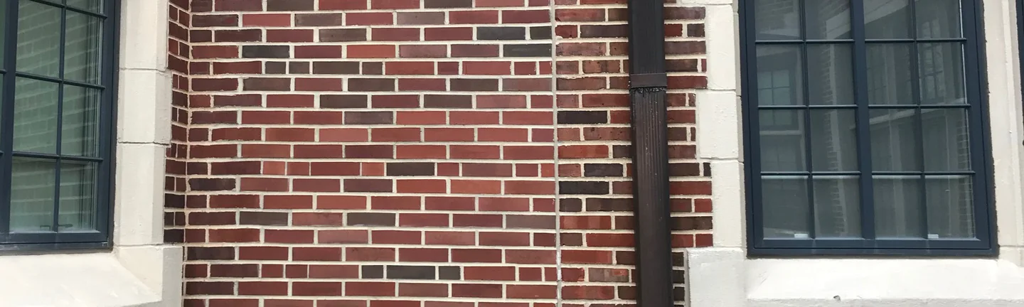 The infill panel beside a downspout on the elementary school in 2020, its red and dark brick reading as one range with the original wall on either side