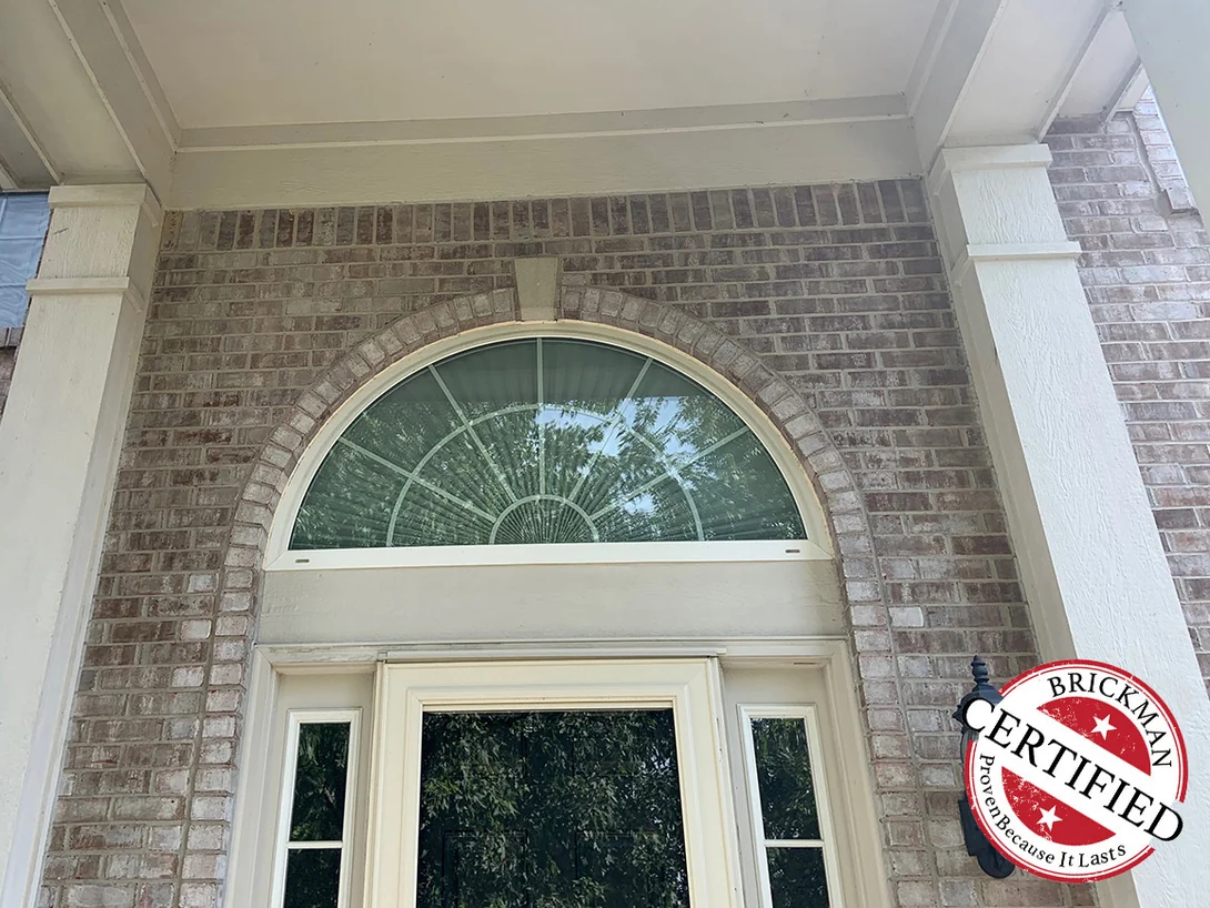 The arched fan window over the front door in 2019, the brick of the entry arch and the wall around it carrying one even tan and cream range, with the Brickman certified stamp in the corner of the frame