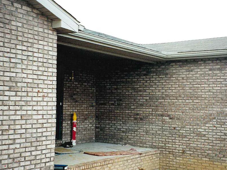 The unfinished front porch corner of the home in 1998, light blotchy brick on both walls, a fire extinguisher and building materials on the slab