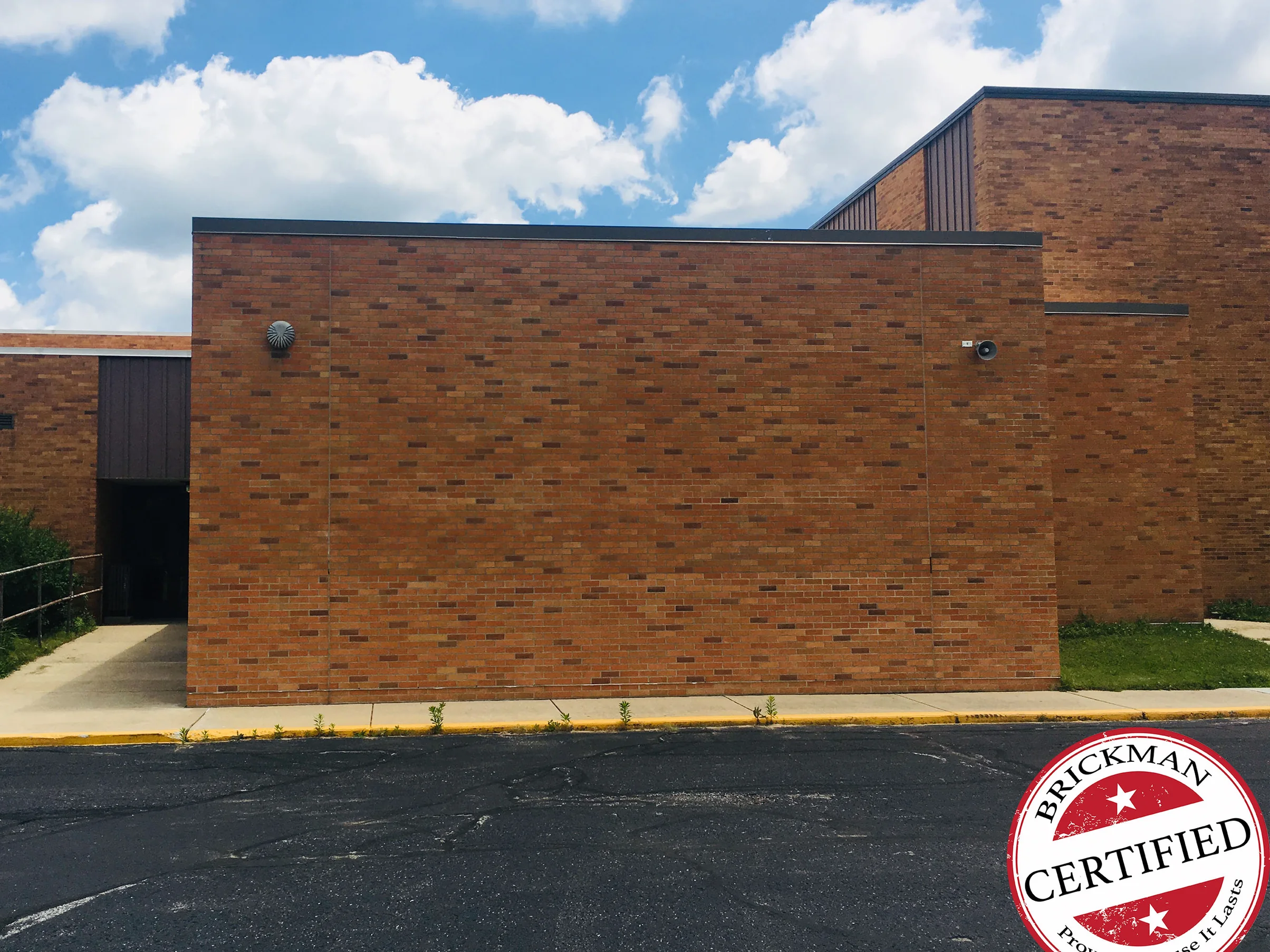 The same wall of the addition in 2019 with the Brickman certified stamp across the corner of the frame, dark units still scattered through the brick