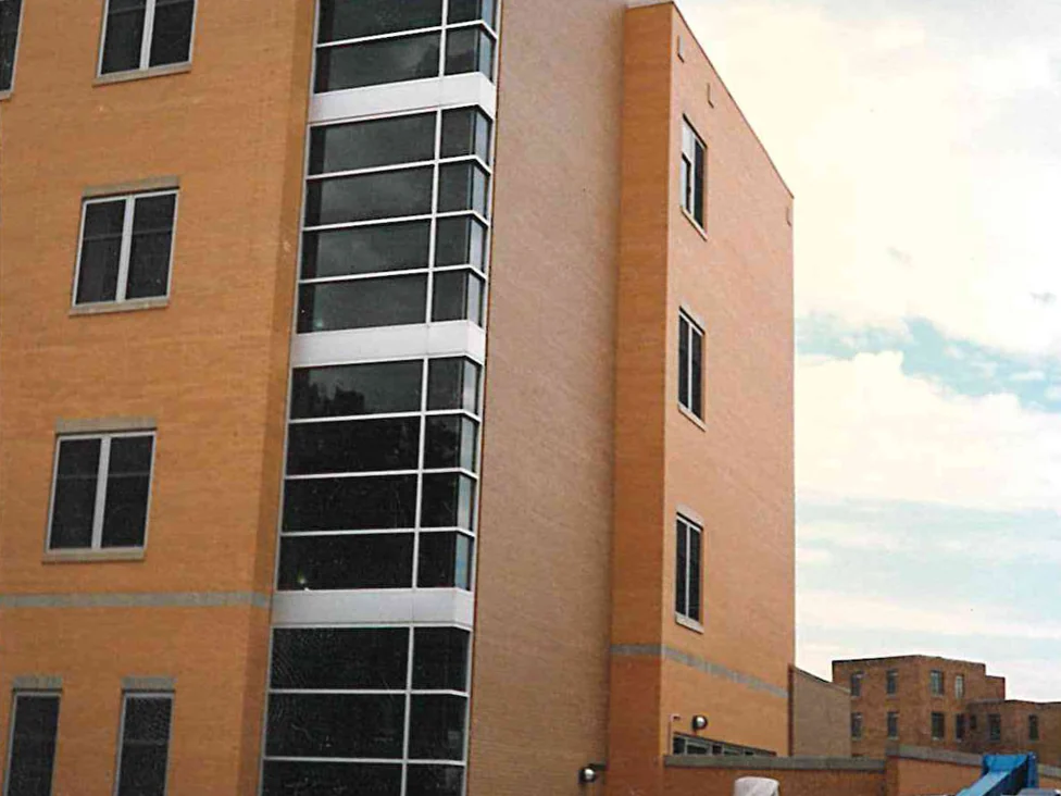 The same corner of the hospital during the 1996 work, a glazed stair tower running the full height beside the wall and a boom lift parked on the fill at the right
