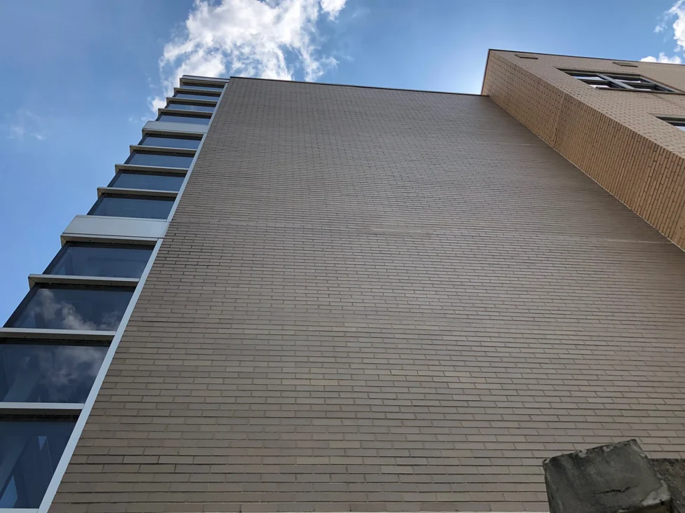 The top of the stained wall in 2019 seen from directly beneath it, the brick running unbroken up to the coping with the ribbon windows of the stair tower down the left edge