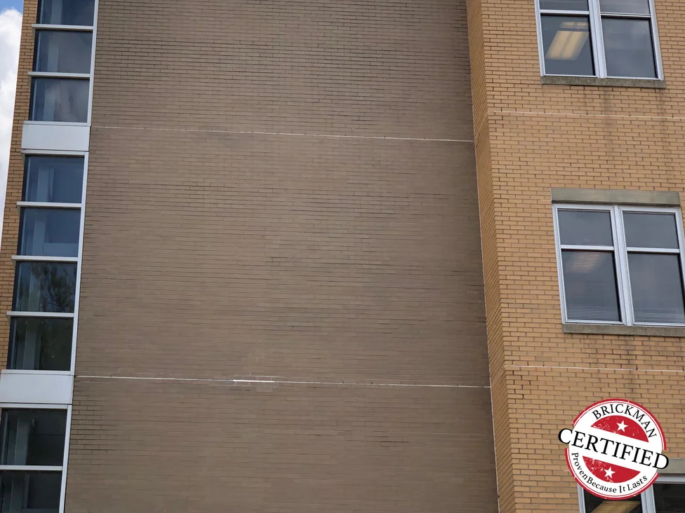 The stained wall square on in 2019 carrying the Brickman Certified stamp, the brick even across the face with a faint horizontal line where the shelf angle runs