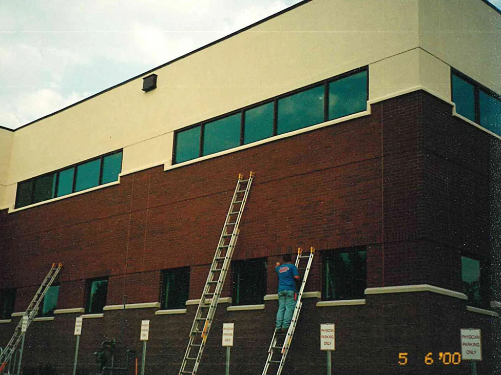 Three ladders against the corner of the two-story office in 2000, an applicator at work on the dark red brick above a row of parking signs