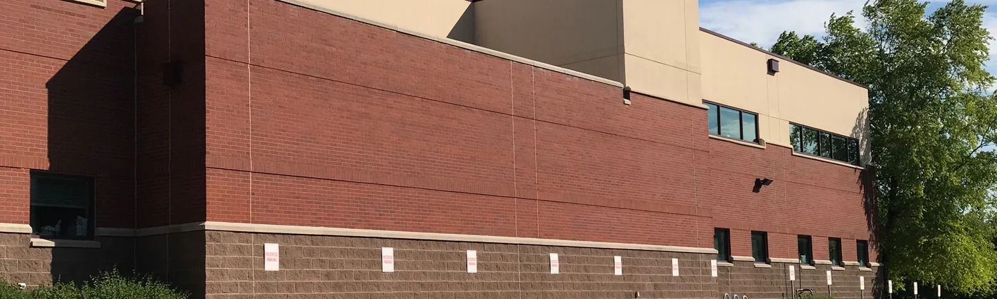 The long back wall of the orthopedics office in 2019, one even range of red brick above a split face block base