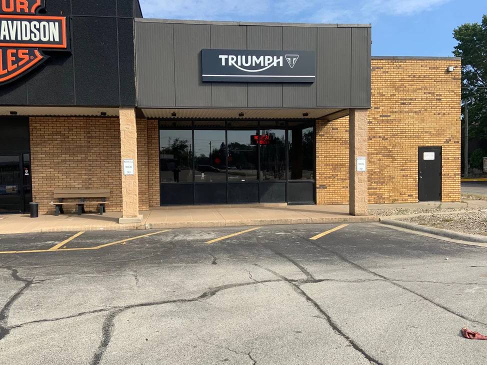 The front of the showroom in 2019, its stained brick piers and walls running past the entrance under the Harley-Davidson and Triumph signs.