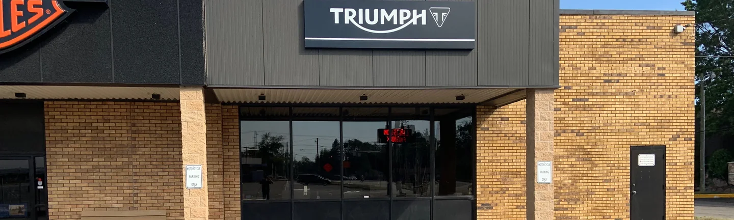 The front of the motorcycle showroom in 2019, its stained brick piers and walls reading as one tan and orange range