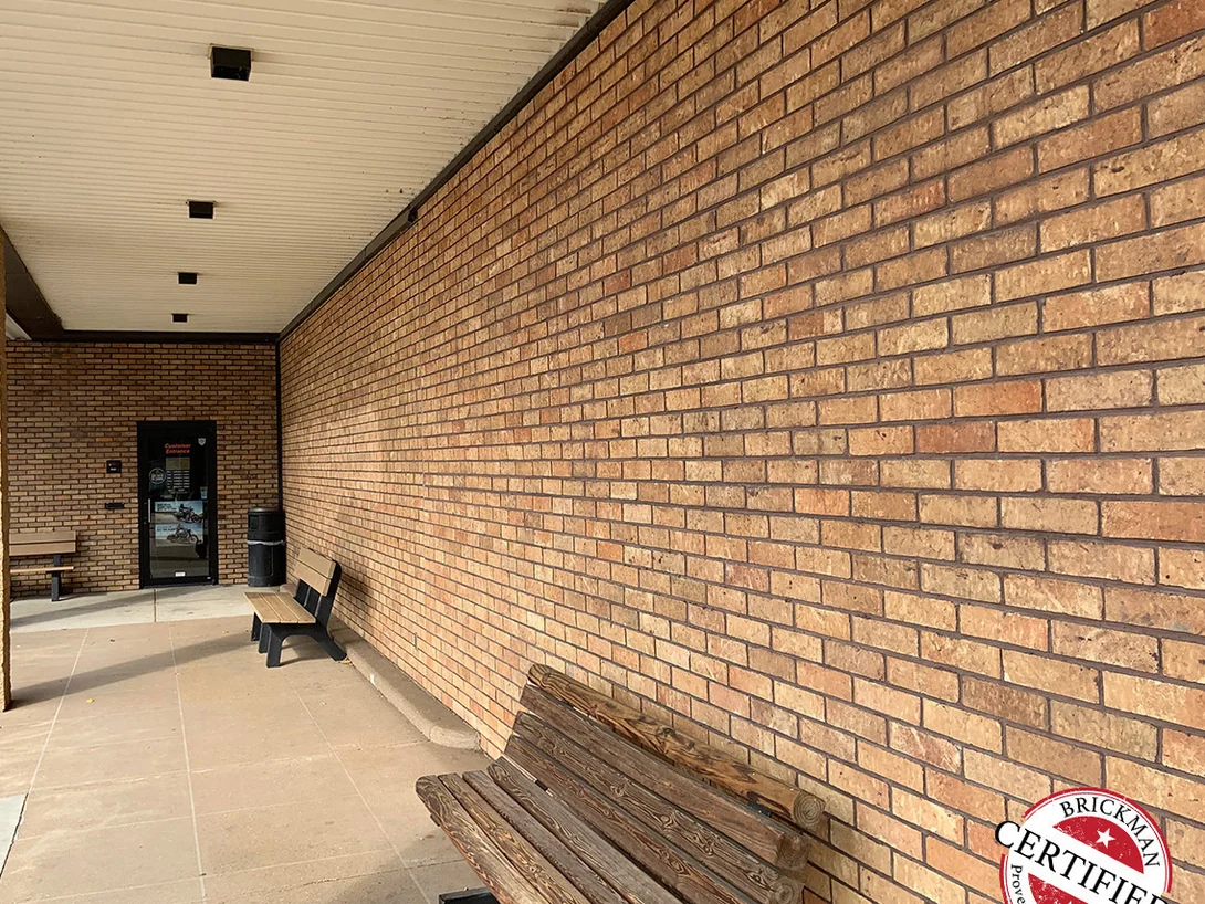 The covered walkway along the showroom in 2019, its brick reading as one tan and orange range past benches and the customer entrance